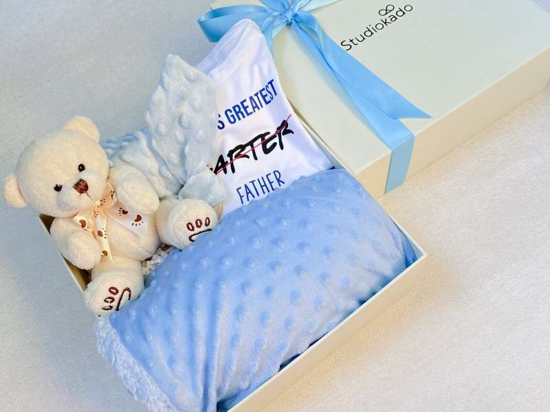 Giftbox filled with warm and soft baby blanket, clothes, baby teether, and a stuffed teddy as a gift for newborns